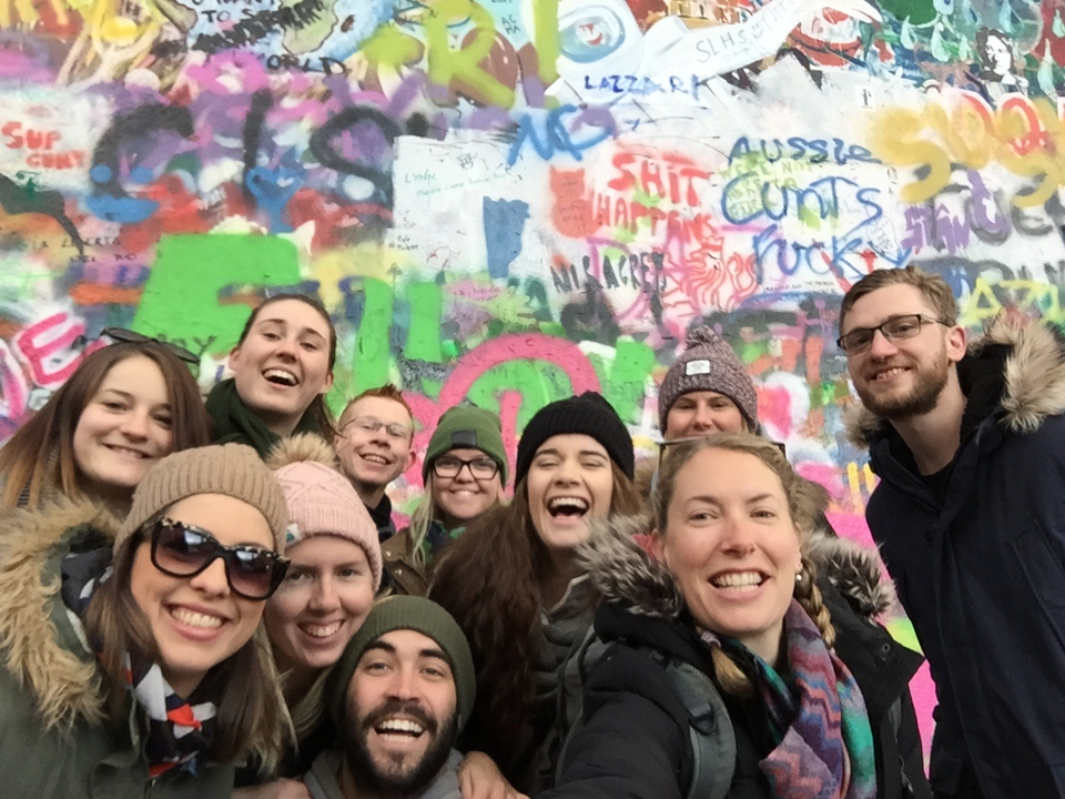 Group of people laughing in front of a colorful graffiti wall.