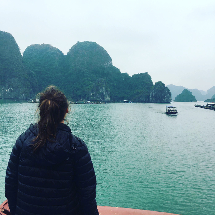 Person observing calm waters and distant karst formations.