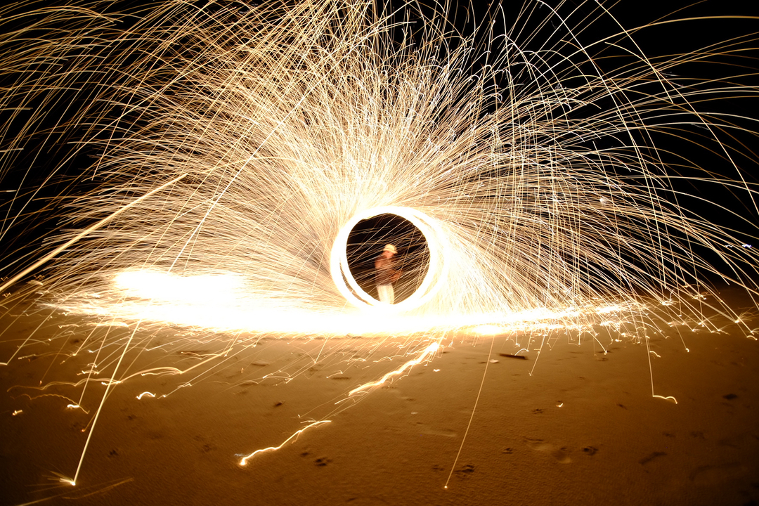 Man performing fire spinning on a sandy beach at night.