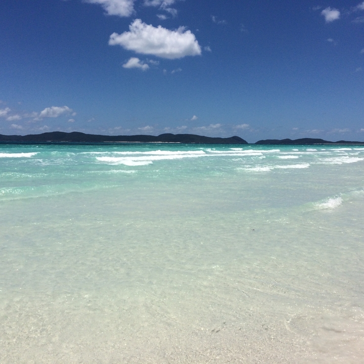 Eau turquoise sur une plage de sable avec des collines au loin.