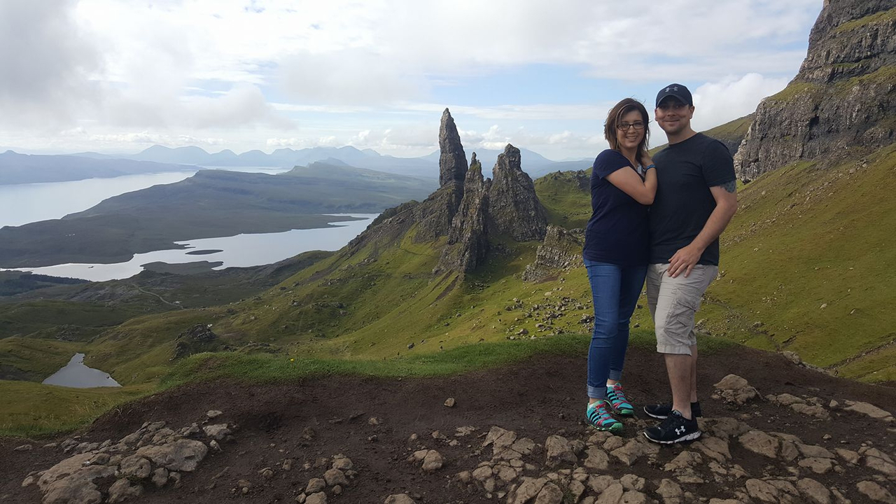 Couple posing in front of dramatic mountain peaks and a lake.