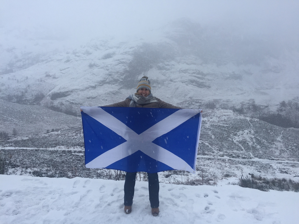 Person holding a Scottish flag in a snowy landscape.