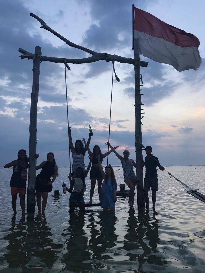 Group of people on swings by the water at sunset.