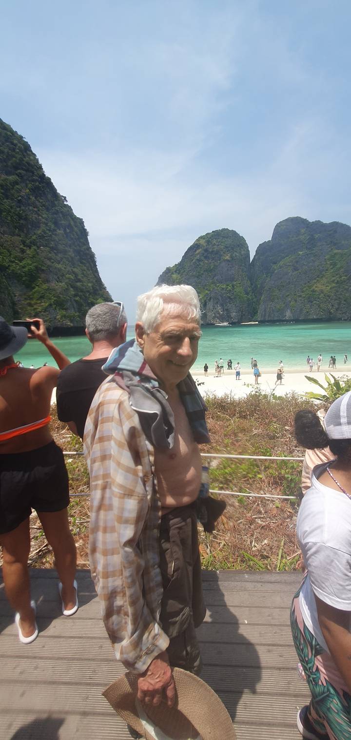 People on a boardwalk by the beach with scenic cliffs.
