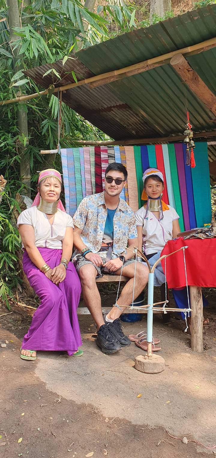 Three people in front of a colorful woven display outdoors.