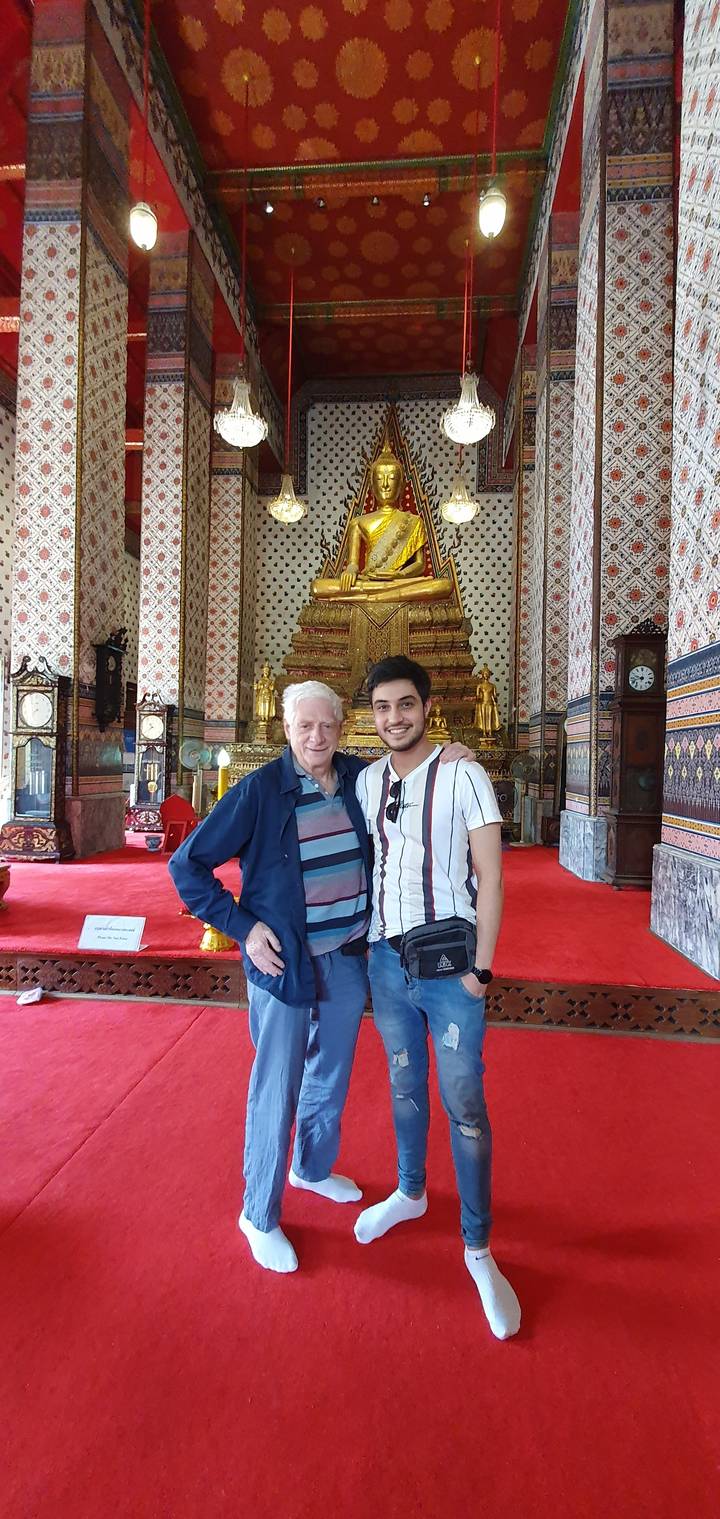 Two people posing in a temple with red carpet and golden altar.