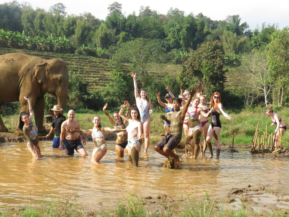 People playing with an elephant in a muddy area.