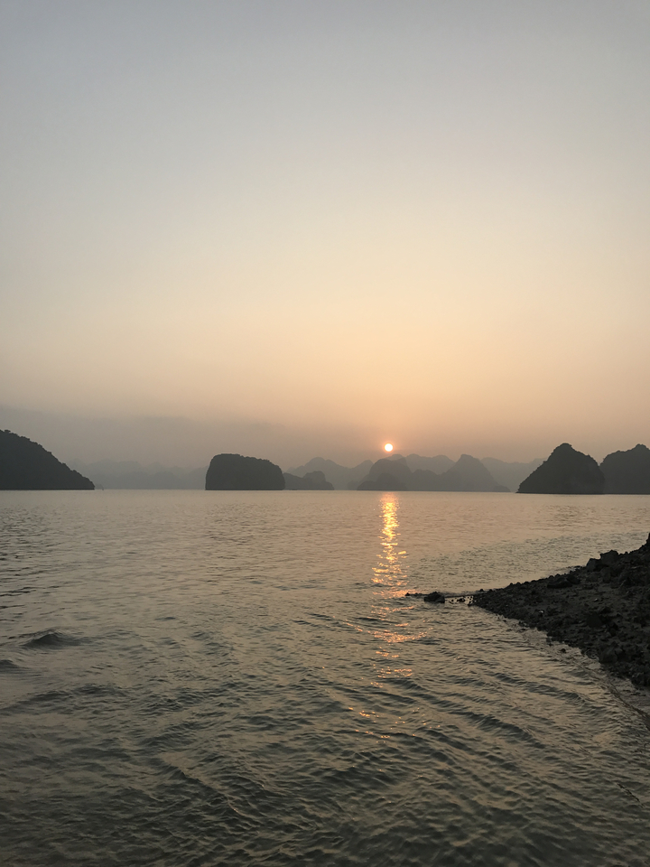 Sunset view over Halong Bay with calm water and rock formations.