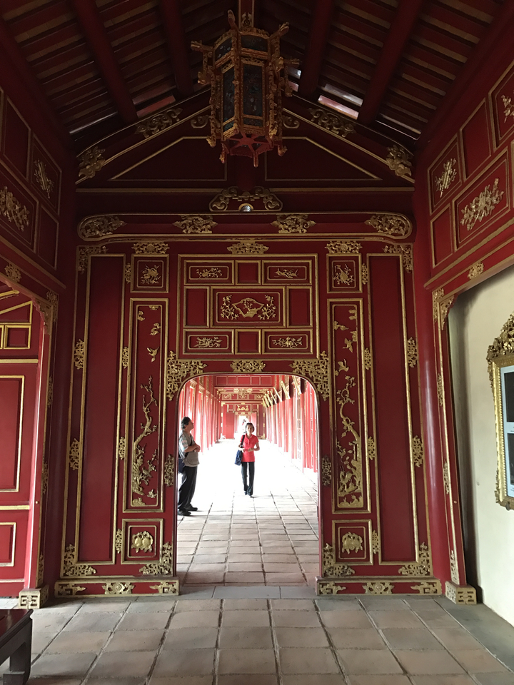 People walking through a red and gold corridor with elaborate carvings.