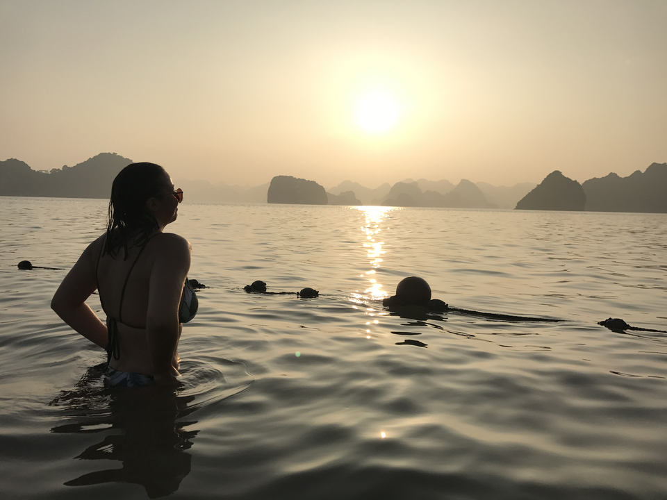 People swimming in a scenic bay during sunset.
