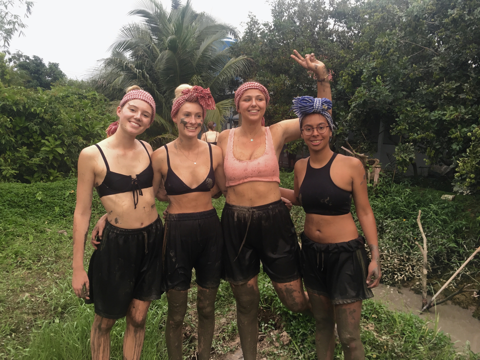 Four women posing with muddy clothes in a jungle area.