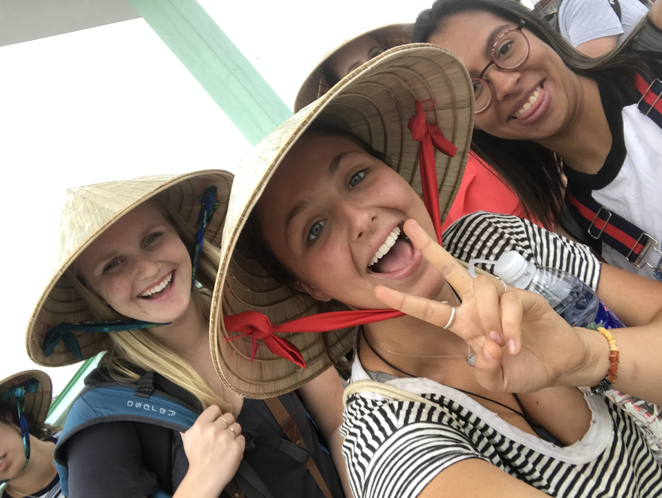 Smiling group wearing conical hats on a boat.