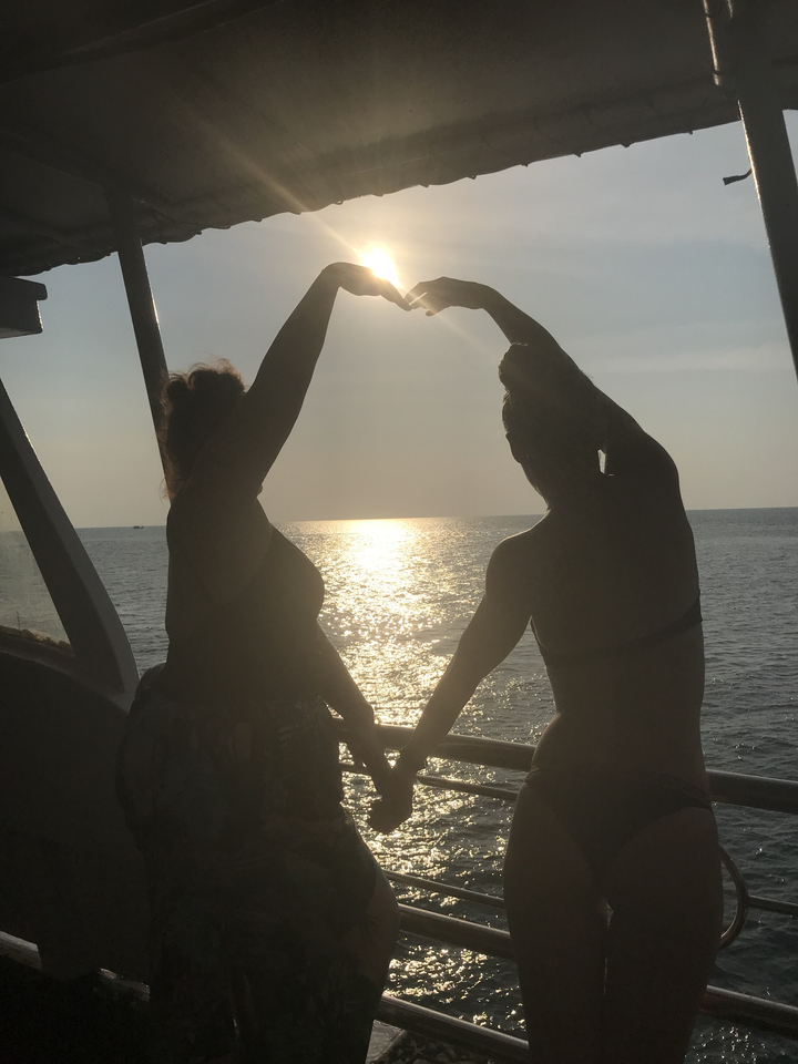 Two women silhouetted against the setting sun on a boat.