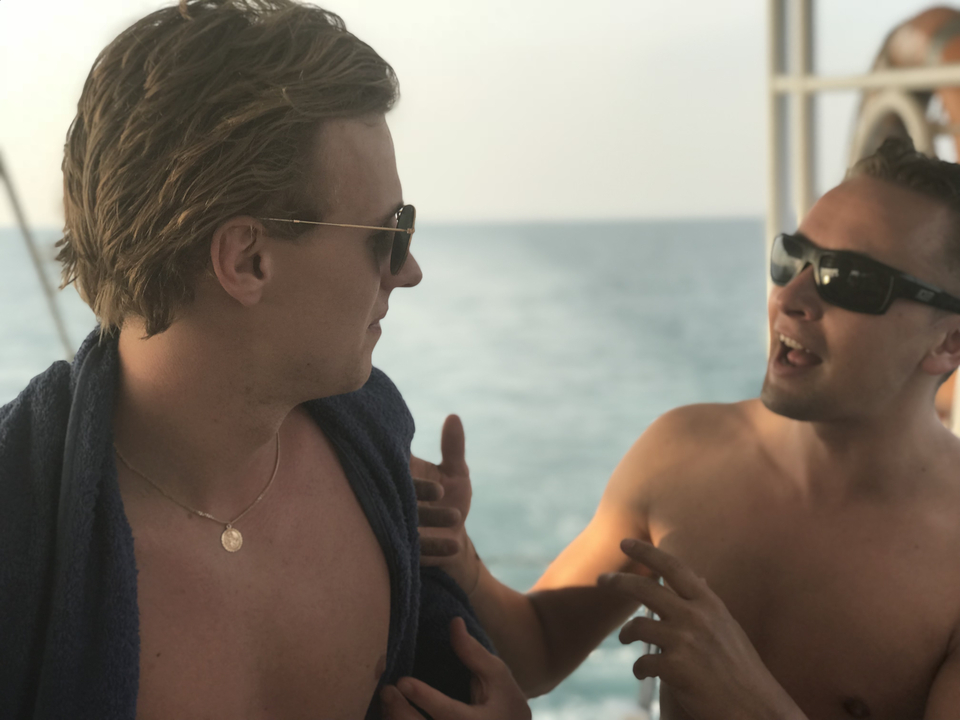 Two men talking on a boat with the ocean in the background.