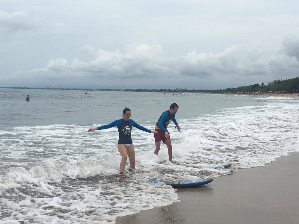 Two people stepping off their surfboards in shallow water.