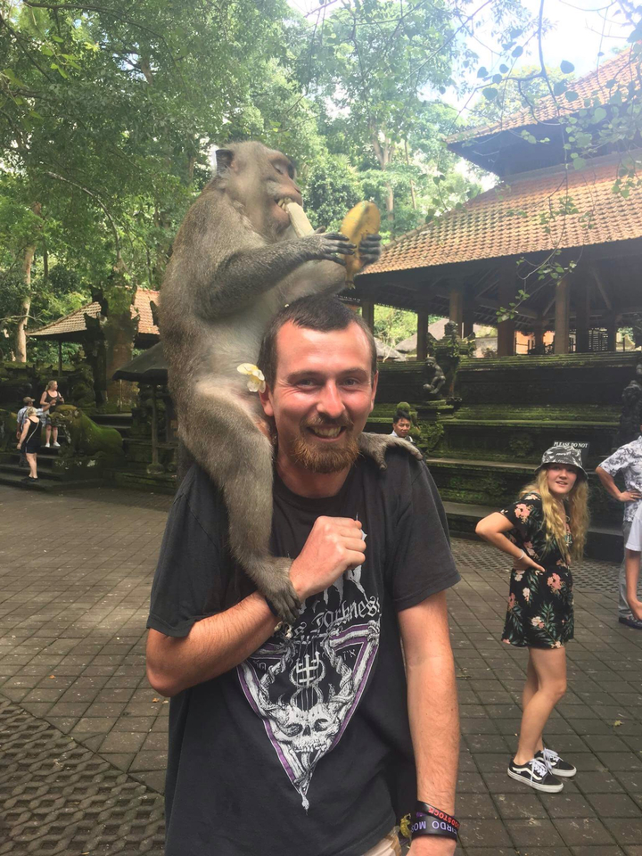 Man smiling with a monkey on his shoulders in a park.
