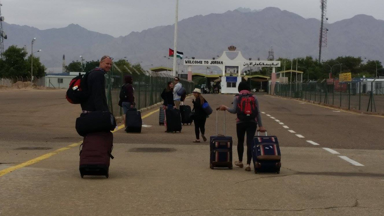 People walking towards a border checkpoint with luggage.