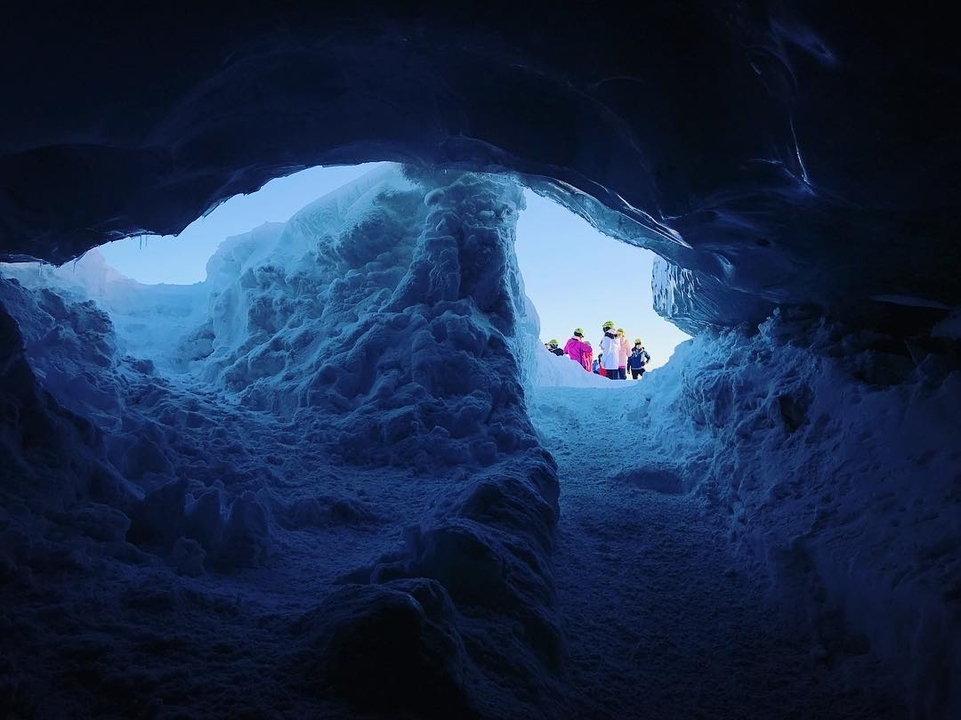 People exiting a cave covered in snow and ice.