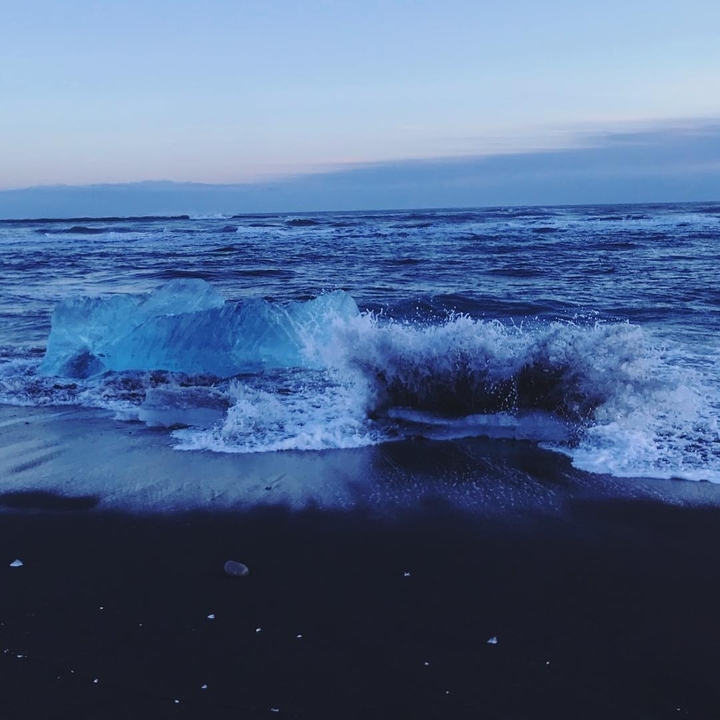 Waves crashing against ice blocks on a beach.