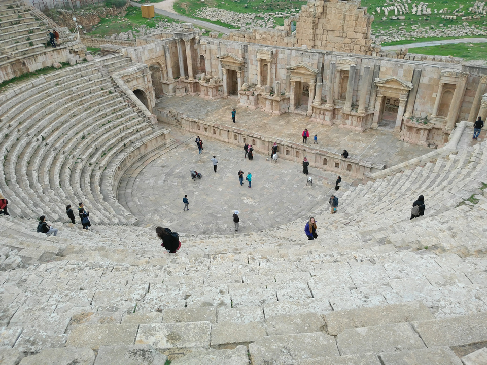 Ancient amphitheater with scattered visitors on steps.