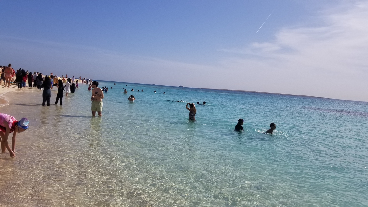 People swimming at a crowded beach on clear day.