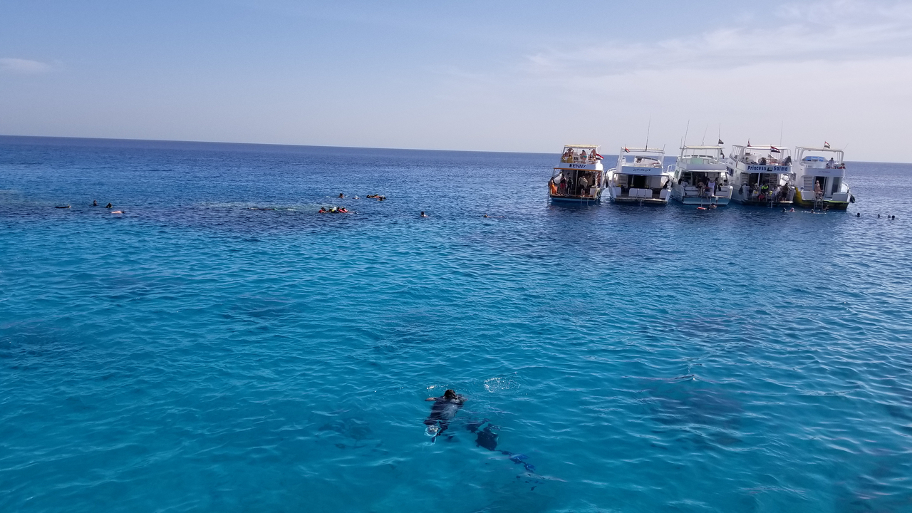 Snorkelers and boats in clear blue ocean.