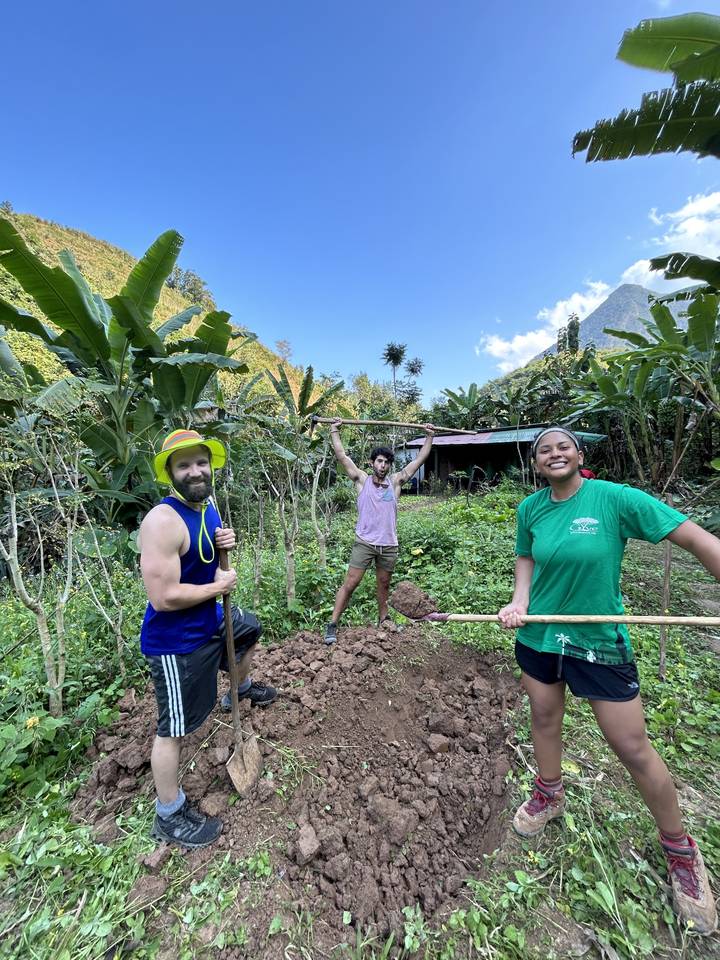 Three people with gardening tools posing in a garden.