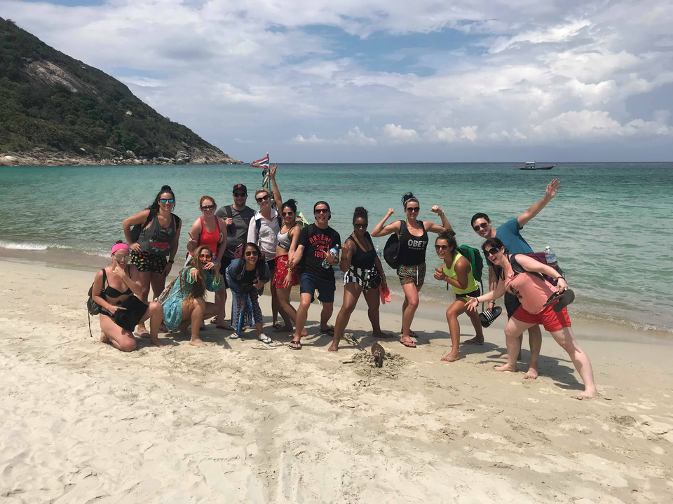 Group posing with arms raised on a beach.