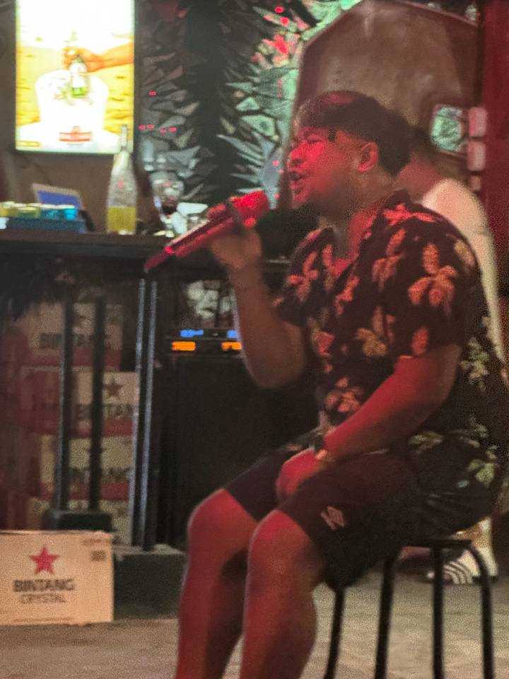 Person singing into a microphone in a dimly lit setting.