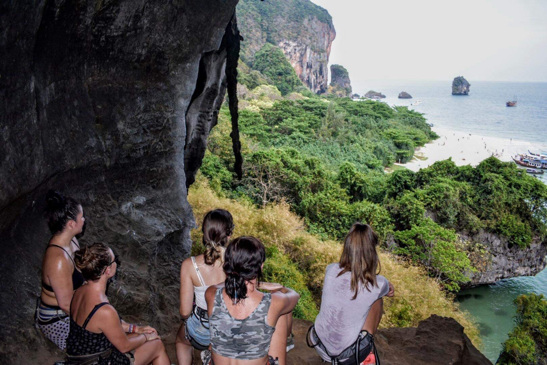 Group of people sitting in a cave with a view of a green coastline.