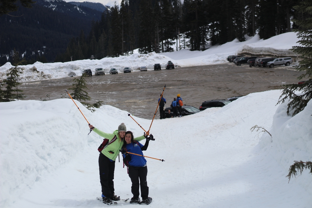 Two people posing with ski poles in a snowy parking lot.