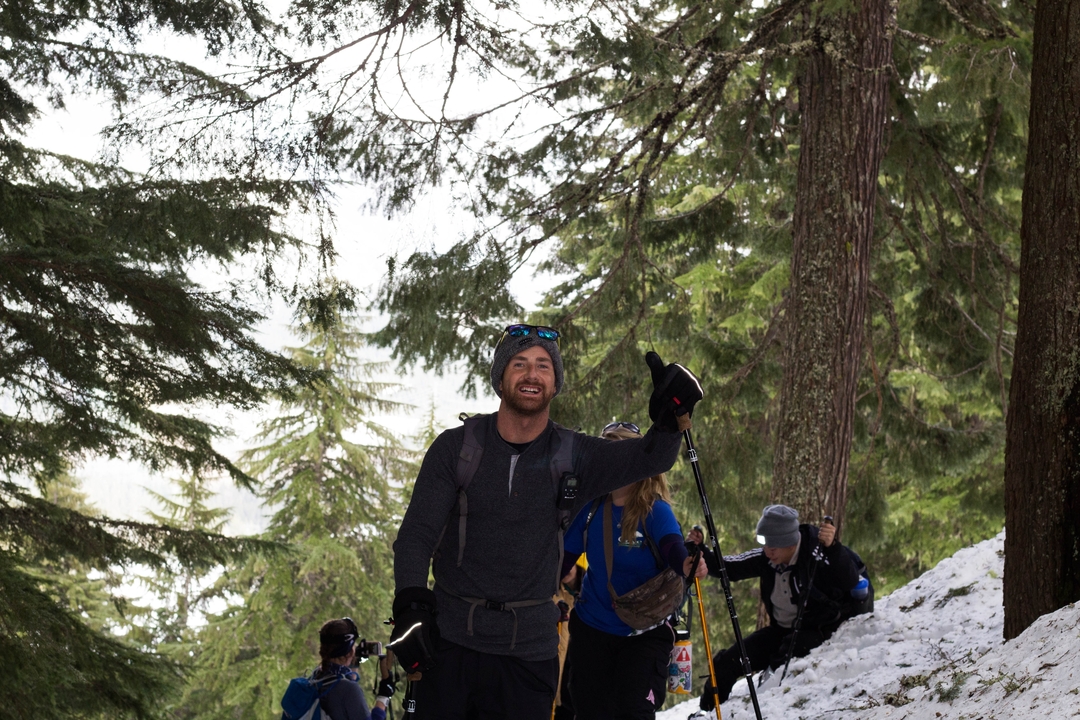Man smiling with hiking gear in a snowy forest.