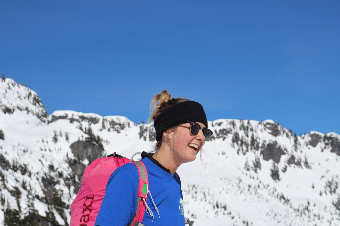 A person with sunglasses and a pink backpack in a snowy mountainous area.