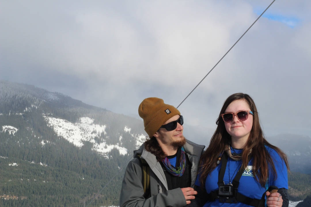 Two people posing with snowy mountains in the background.