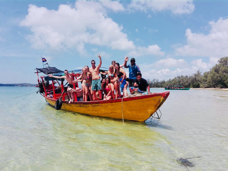 Group of people posing on a yellow boat in clear shallow water.