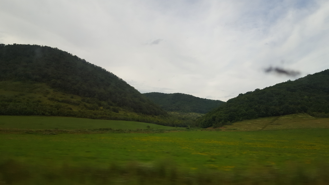 Rolling hills and green fields under a cloudy sky.