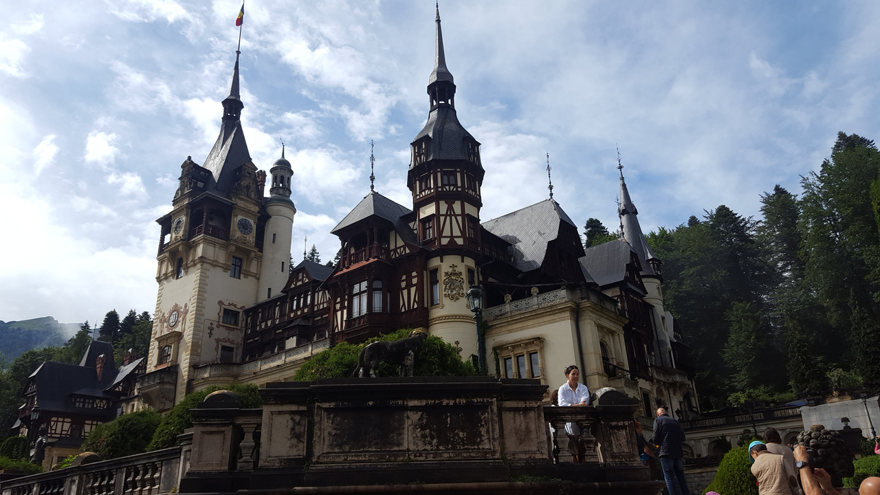 Peles Castle with Gothic architecture and surrounding evergreen trees.