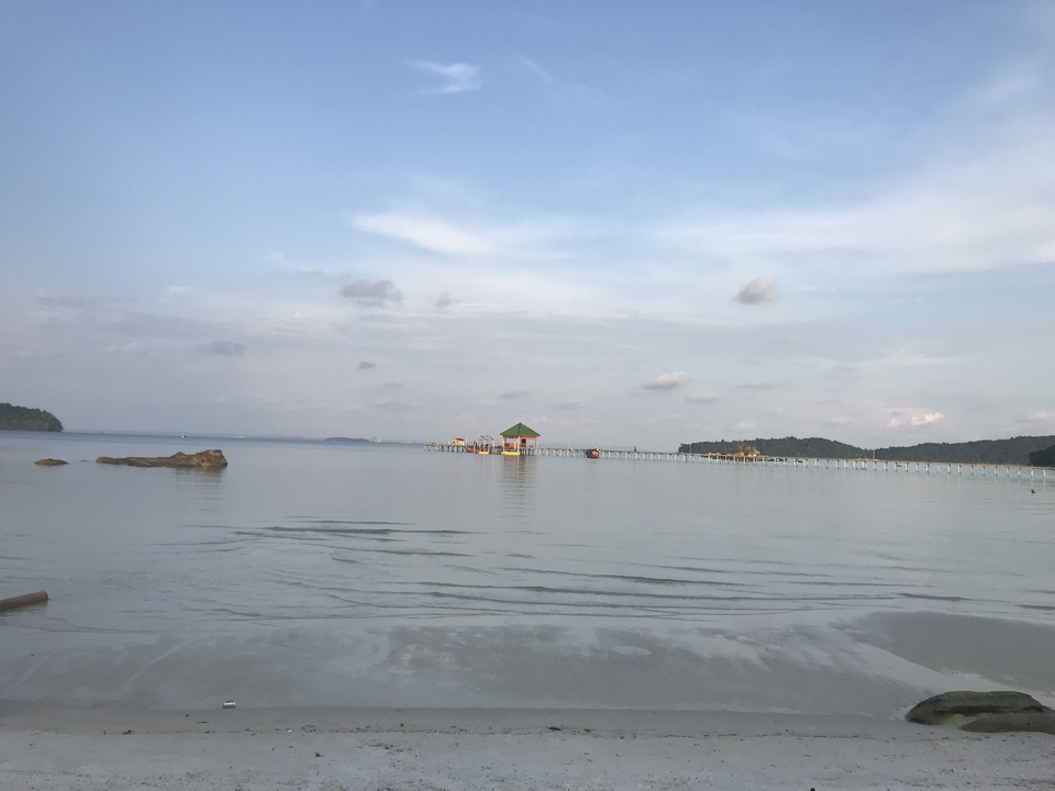 Calm sea with a pier stretching into the distance under a blue sky.