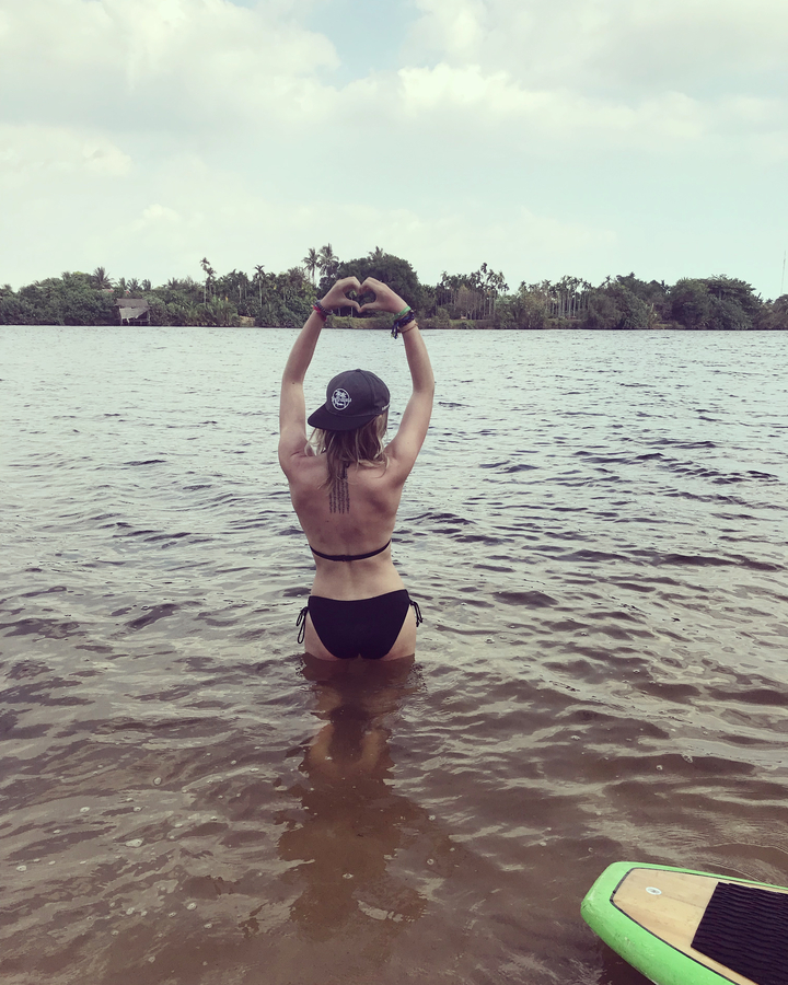 Person standing in water with hands forming a heart shape overlooking the landscape.