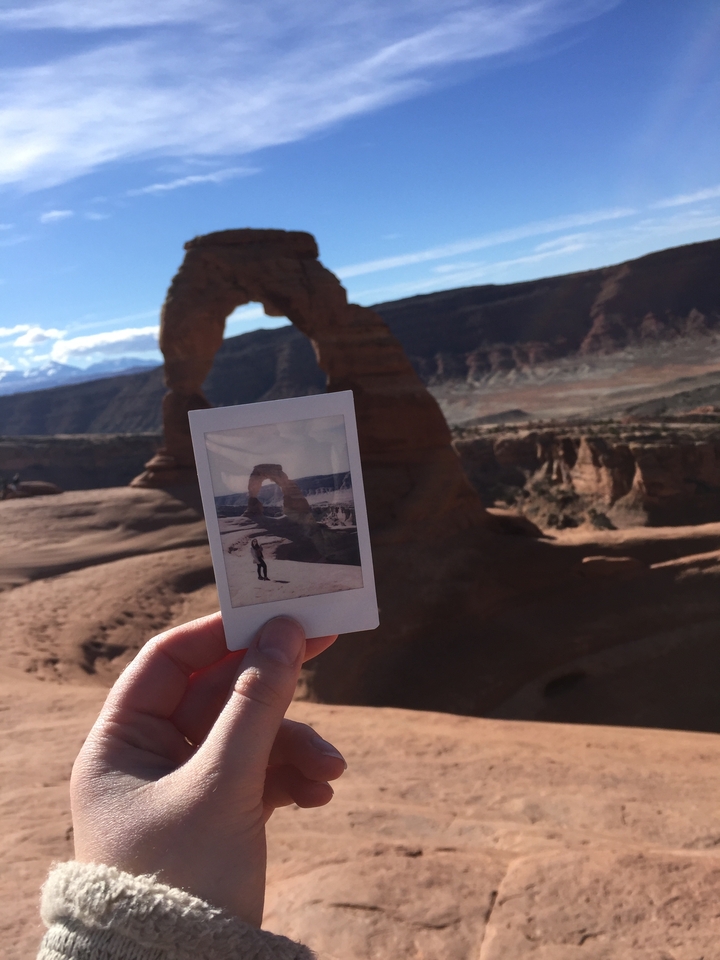 Person holding a Polaroid in front of a natural rock arch.