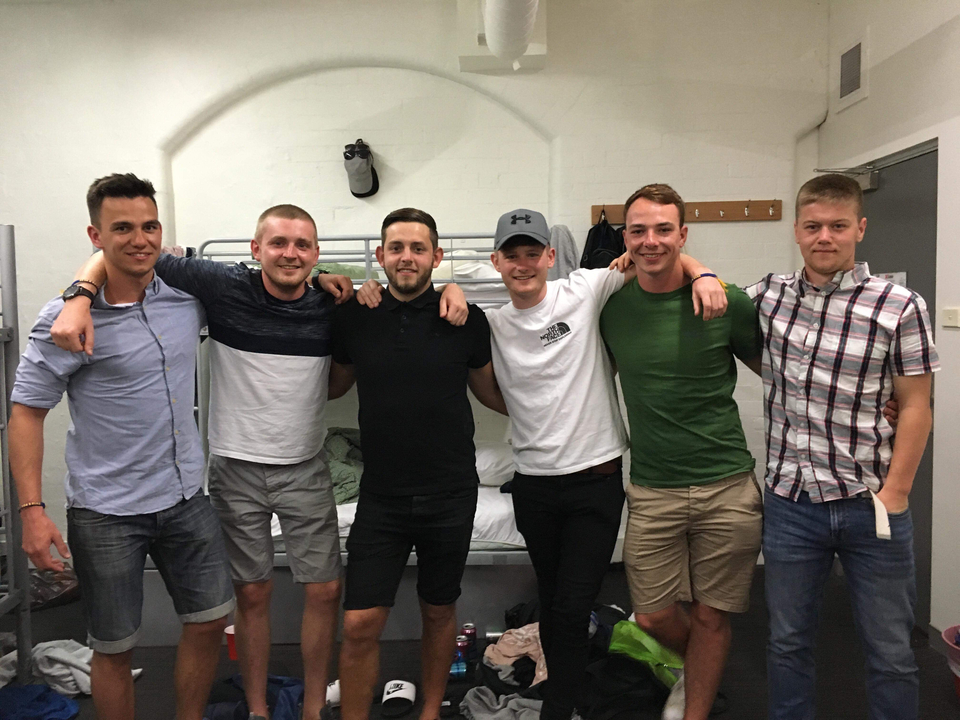 Six friends posing inside a hostel room.