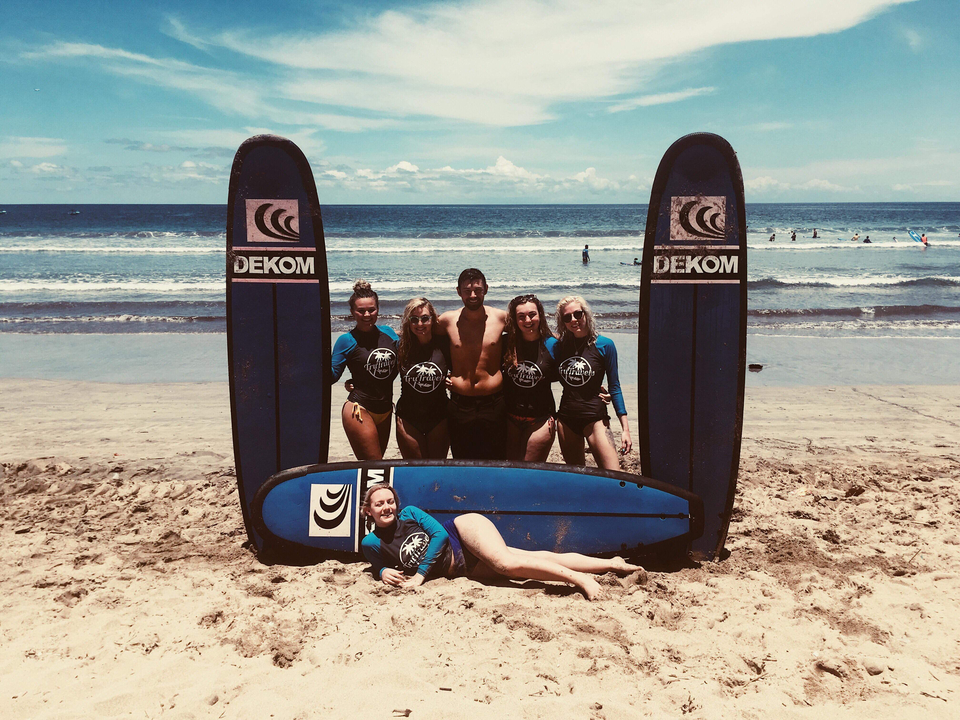 Group of surfers posing with surfboards on a sandy beach.