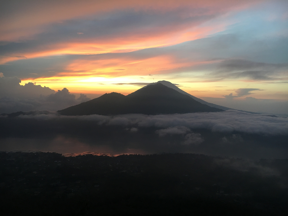 Scenic view of a mountain silhouette at sunset, above clouds.