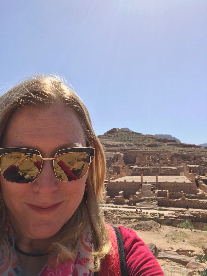 A close-up of a woman with reflections of ancient ruins in her sunglasses.