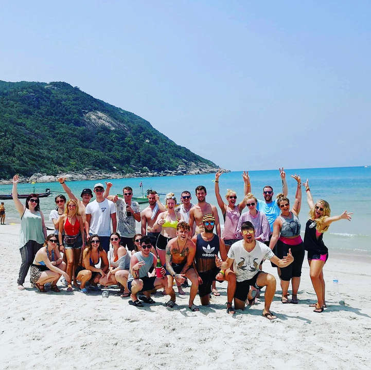 Large group of people cheerfully posing on a beach with clear water