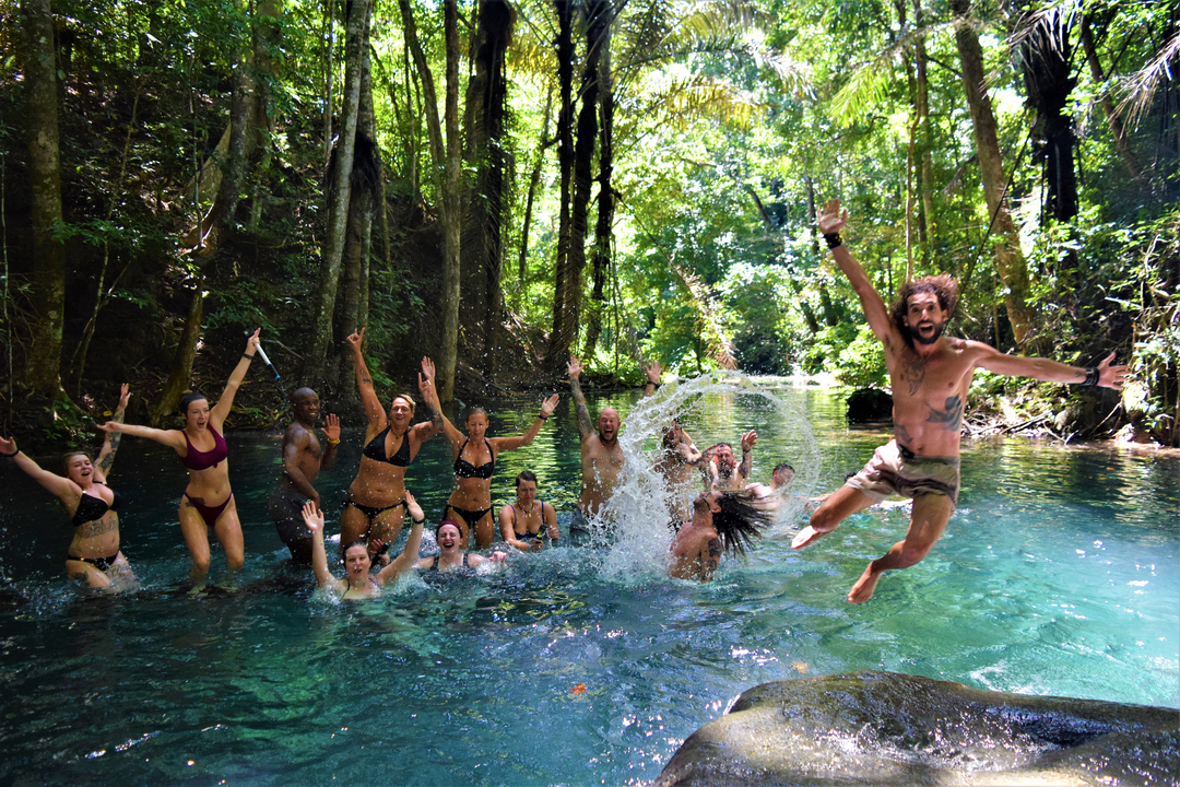 Group of people jumping into a clear river surrounded by lush greenery.