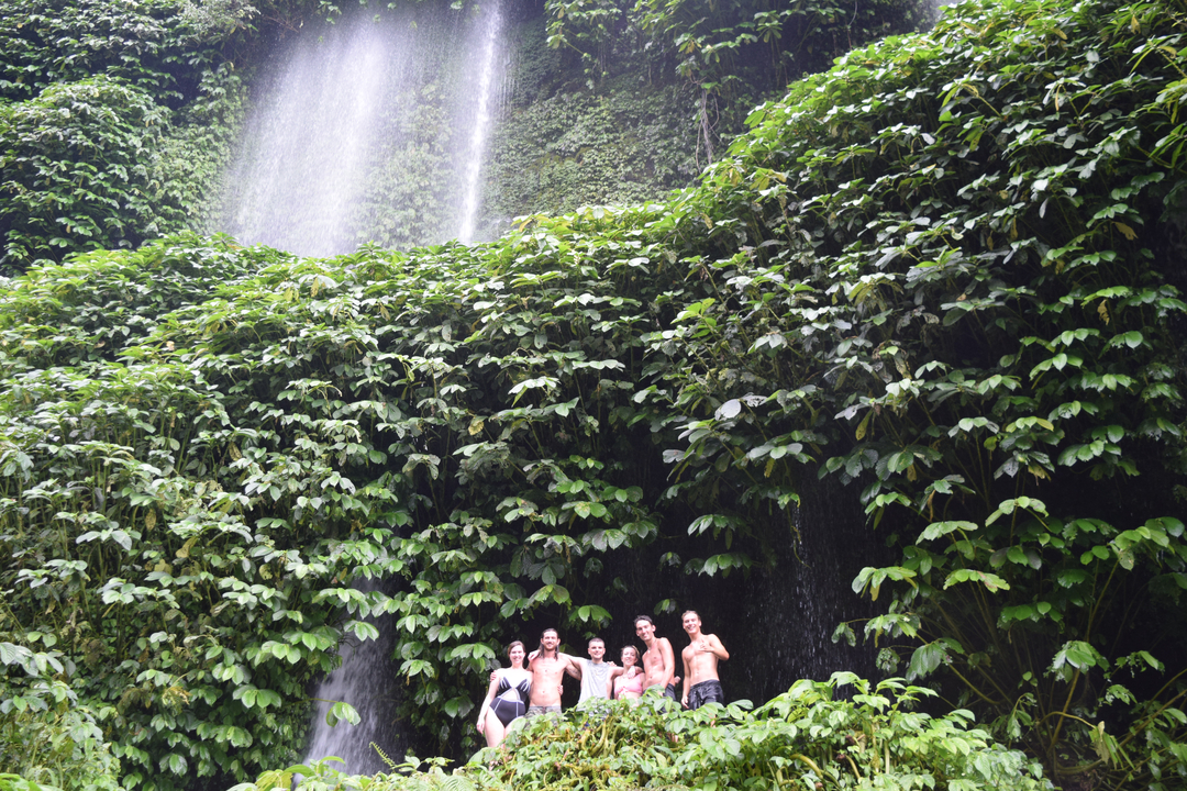 Group of people under a waterfall surrounded by lush foliage.