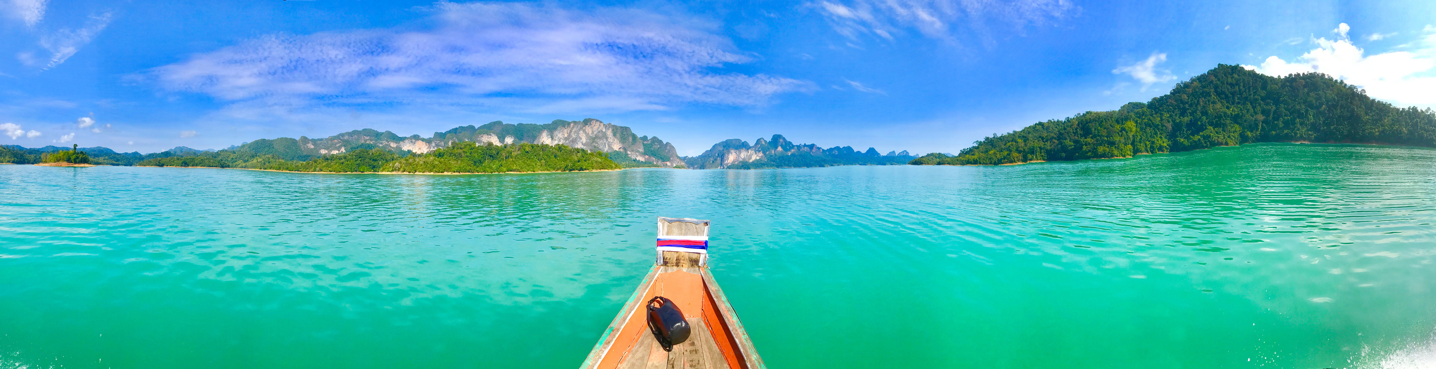 Long tail boat on turquoise water with mountainous background.