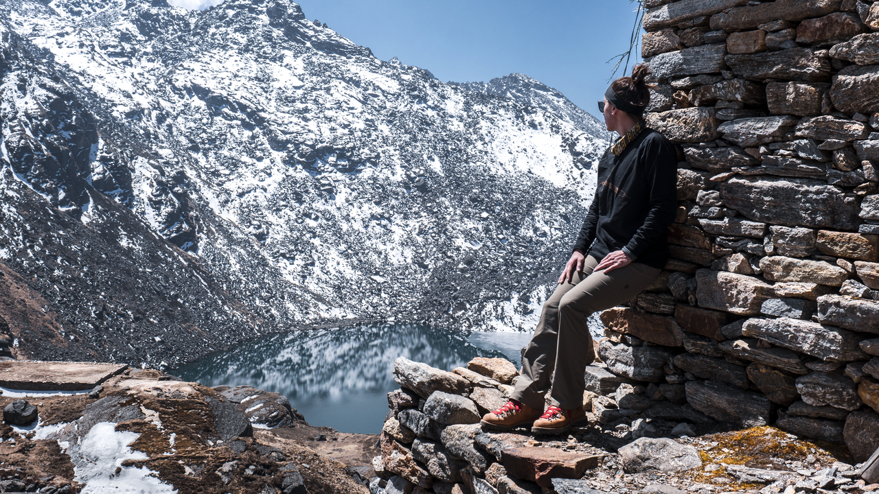 Person sitting on a stone wall overlooking a lake in the mountains.
