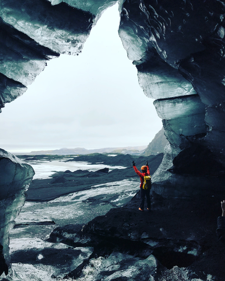Hiker standing at an icy cave entrance.